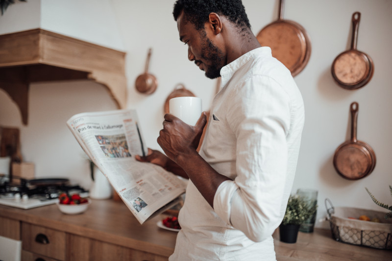 man looking at an advert in a newspaper while drinking coffee